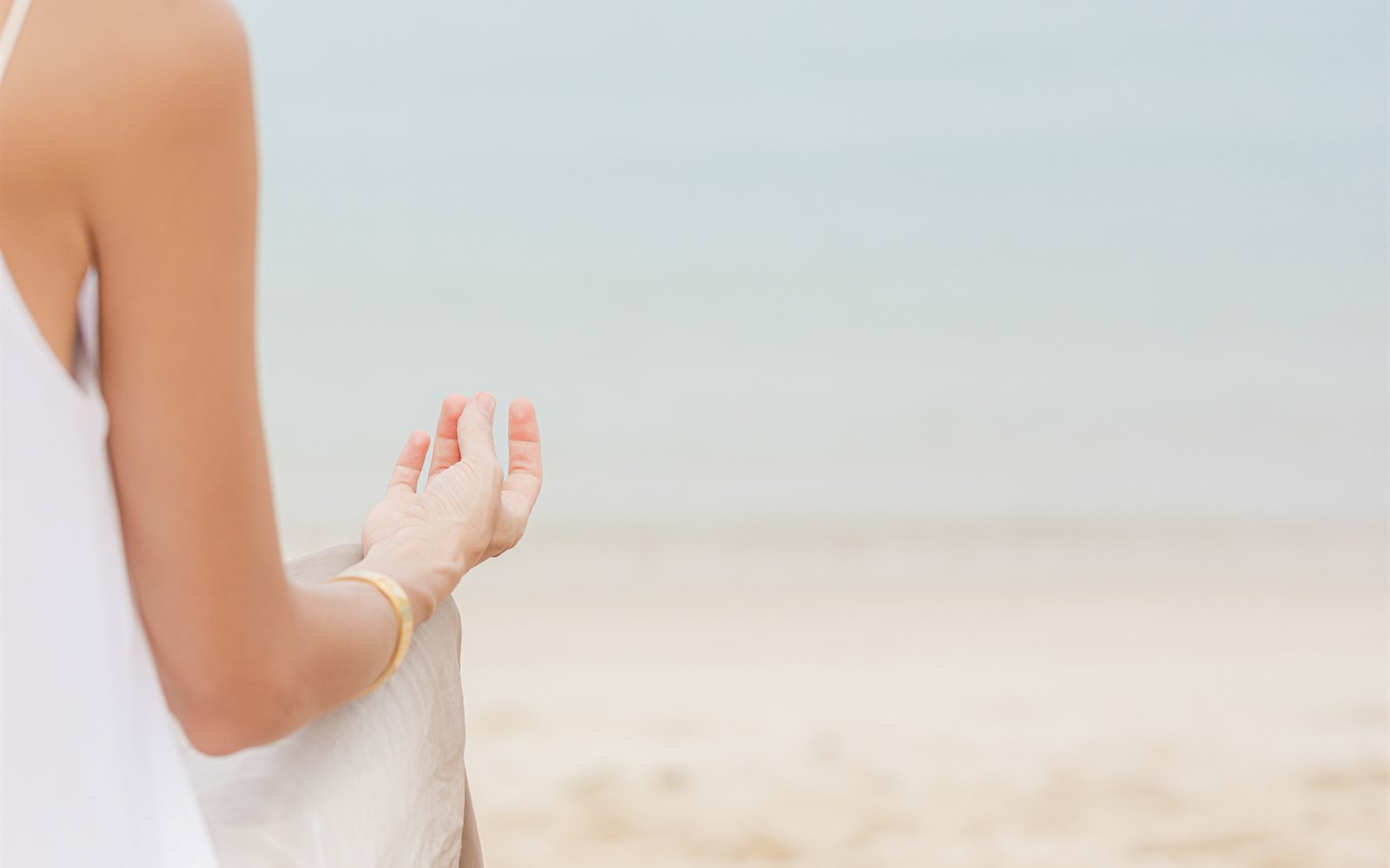 Frau in weißem Kleid meditiert entspannt am Strand, Symbolbild für Blähbauch loswerden und sich wieder leicht fühlen