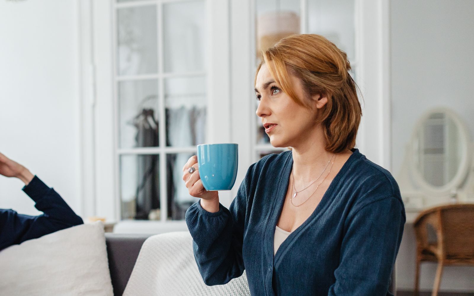 Nachdenkliche Frau sitzt mit einer Tasse in der Hand zu Hause, Symbolbild für eine oft unerkannte Dünndarmfehlbesiedlung