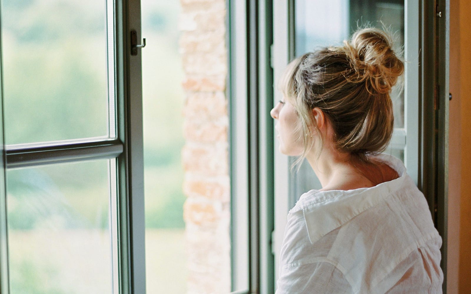 Nachdenkliche Frau schaut aus einem Fenster ins Grüne, Symbolbild für das Nachdenken über die Diagnose Reizdarm