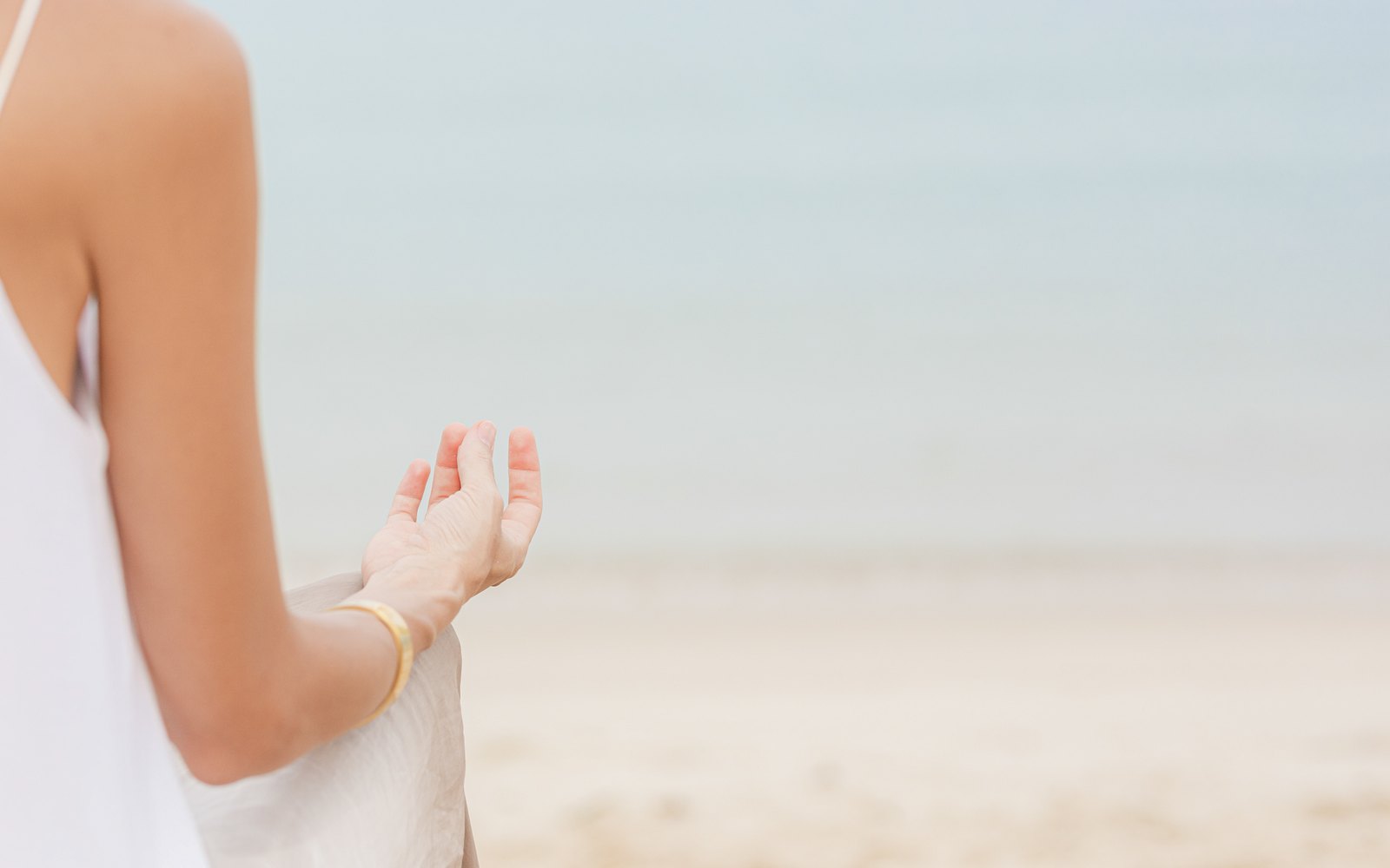 Frau in einem weißen Kleid am Strand, Symbolbild für Verstopfung im Urlaub