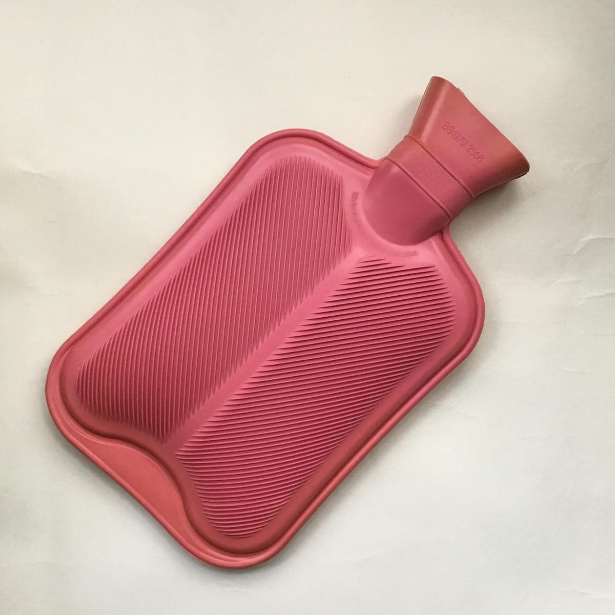 Rosa Wärmflasche für einen Leberwickel beim Fasten auf hellem Untergrund
